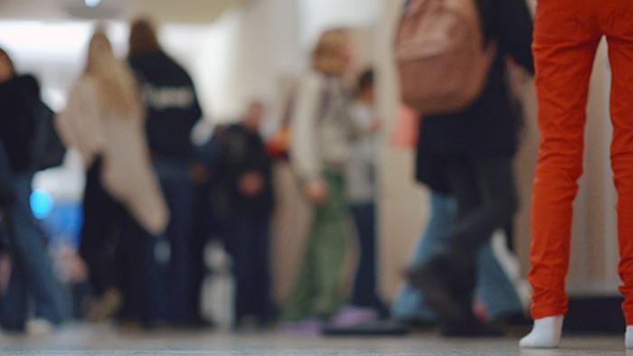 Personer i skolkorridor, i förgrunden ett par ben i orange jeans