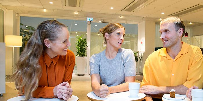 Tre kollegor, två kvinnor och en man, i glatt samtal vid fikabordet