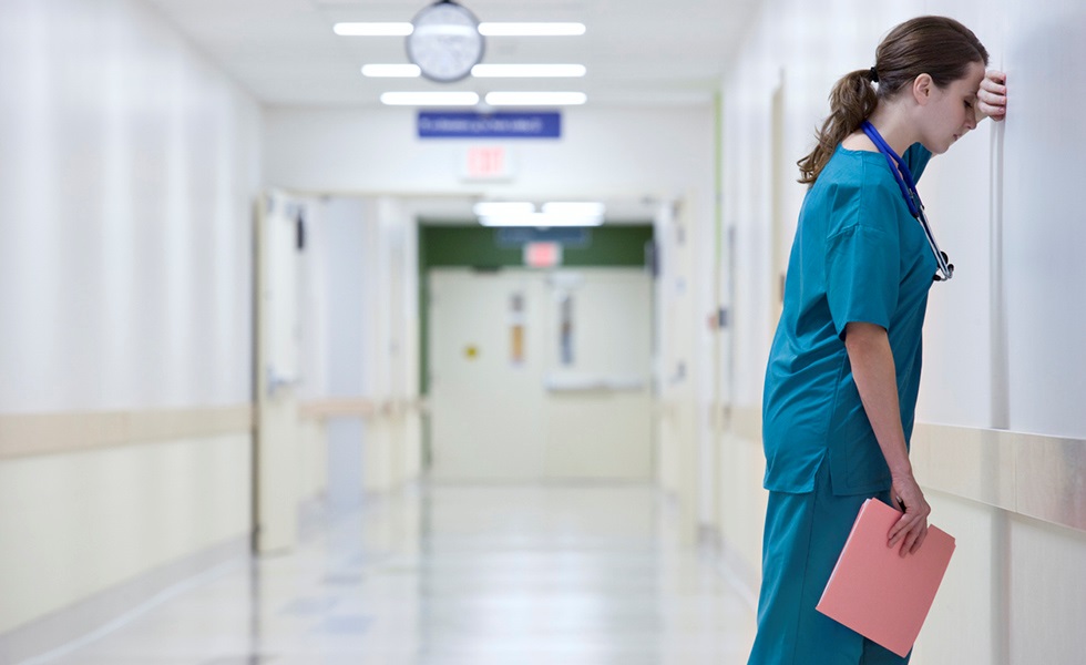 En kvinnlig läkare står lutad mot en vägg i en sjukhuskorridor. 