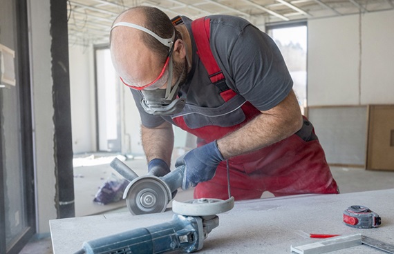 En byggnadsarbetare med andningsskydd skär i en bänskiva.