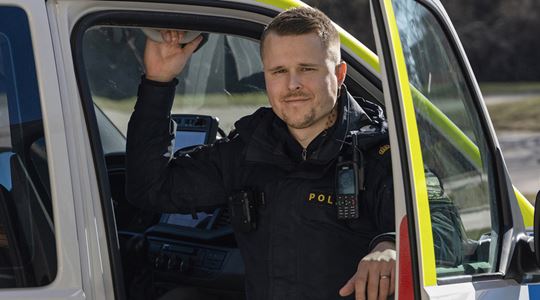Christoffer Nydal, i polisuniform sitter i en polisbil med öppen dörr.