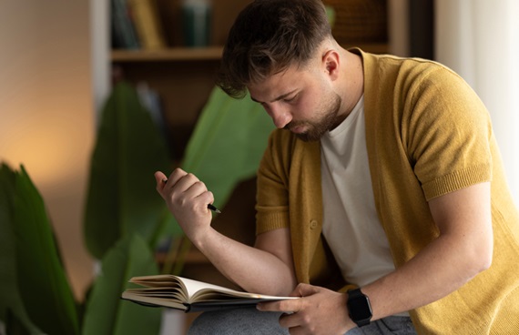 En man sitter böjd över en anteckningsbok med en penna i handen.