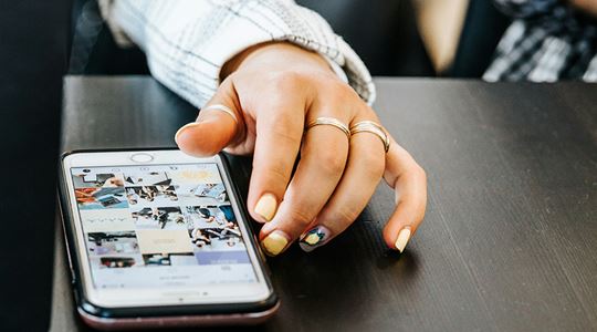 En ung kvinna scrollar bland bilder i mobilen.
